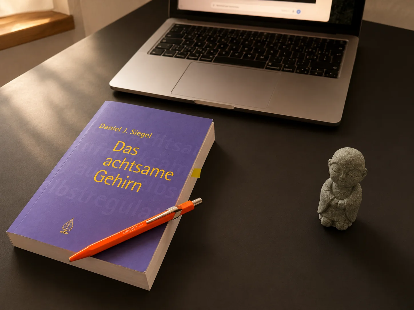 Buch «Das achtsame Gehirn» von Daniel J. Siegel mit Schreibstift und kleiner Buddha-Figur auf dem Schreibtisch